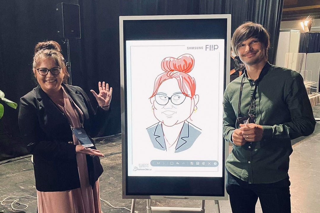 Karikatūrists pabeidzis zīmējumu uz Samsung flip tāfeles un pozē kopā ar uzzīmēto personu