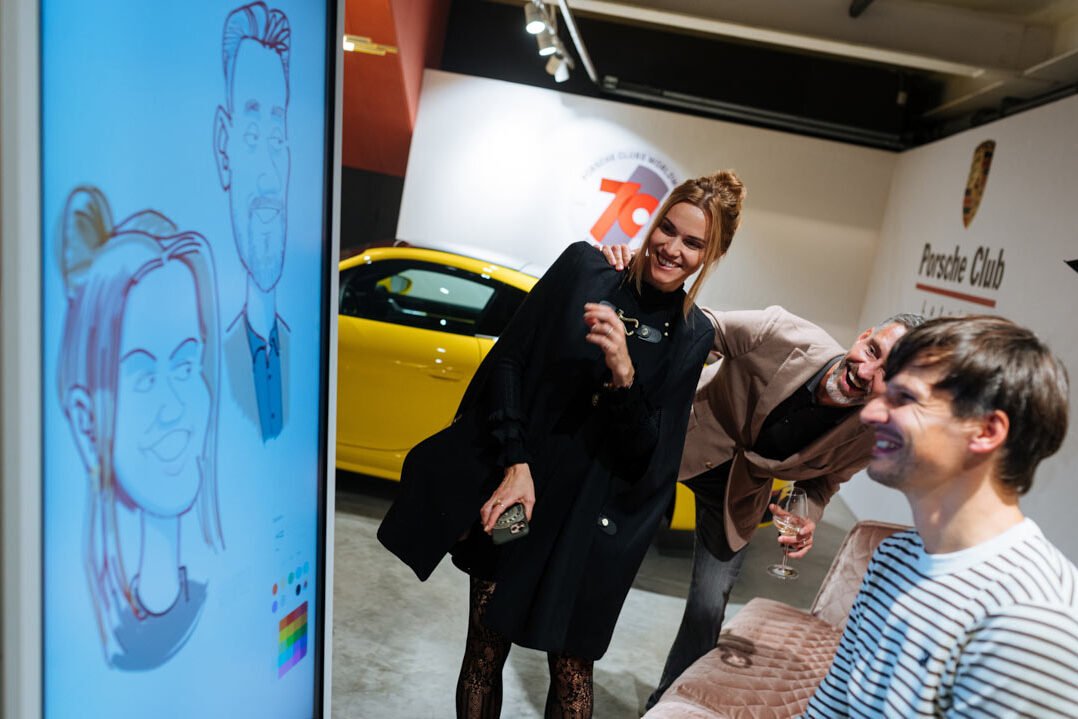 Karikatūrists Gatis Šļūka uzzīmējis pāra karikatūru uz Samsung flip tāfeles un uzzīmētās personas to ieraugot pārsteigumā smaida