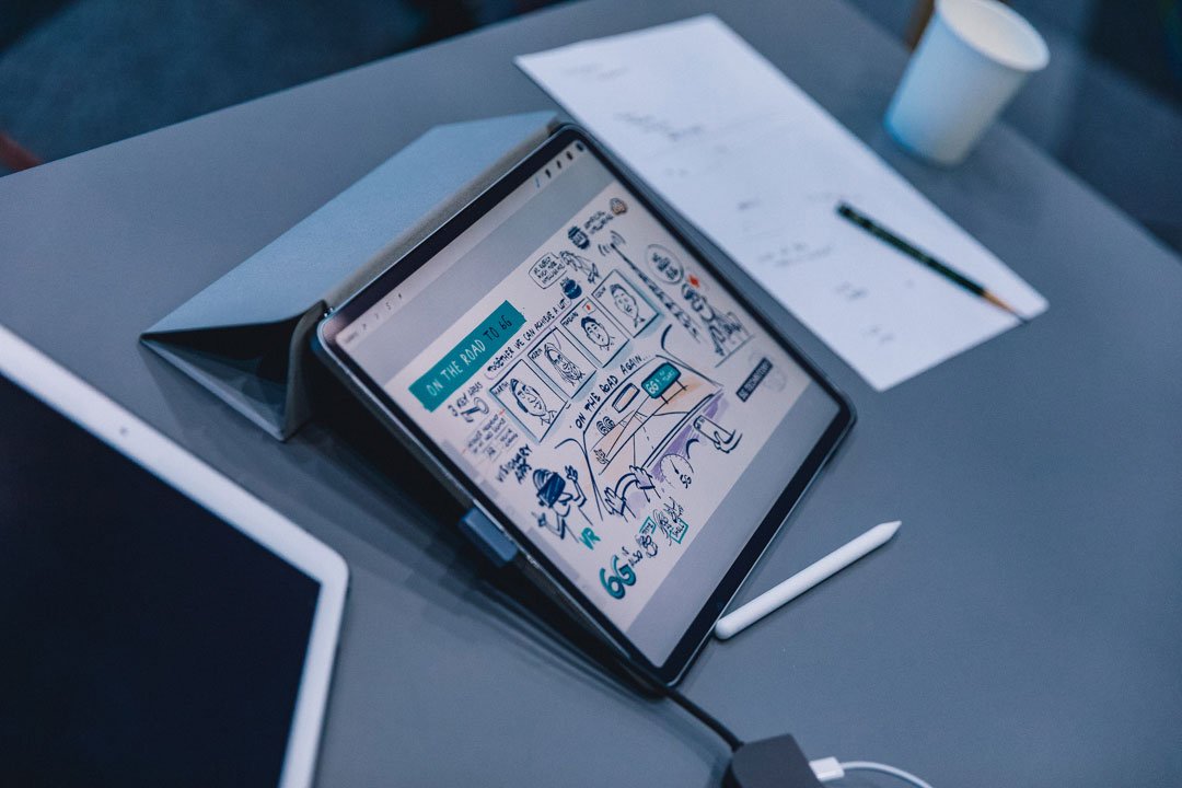 Uz galda iPad Pro, Apple zīmulis, parastais zīmulis, papīra lapa. Tas viss nepieciešams karikatūristam zīmējot konferencē.